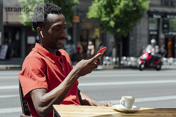 Lächelnder Mann  der im Café sitzt und sein Mobiltelefon benutzt