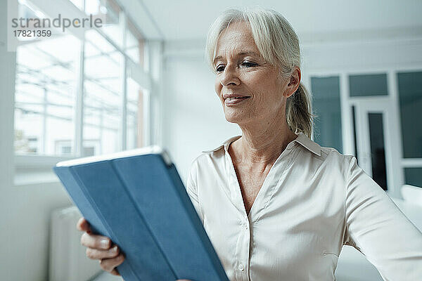 Smiling senior businesswoman holding tablet PC in office