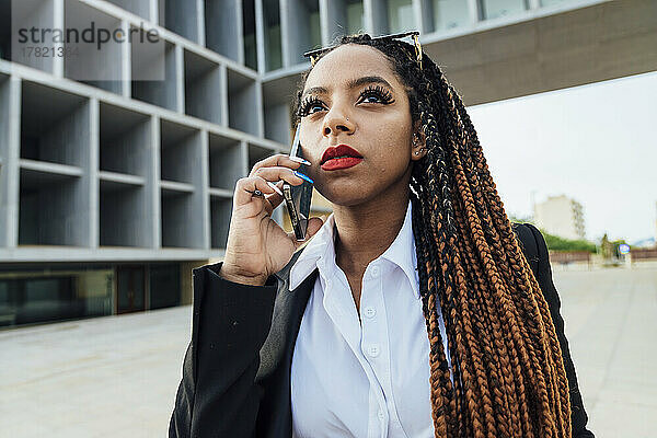 Junge Geschäftsfrau spricht mit Smartphone vor Bürogebäude