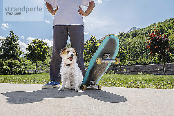 Mann mit Hund und Skateboard steht auf der Straße