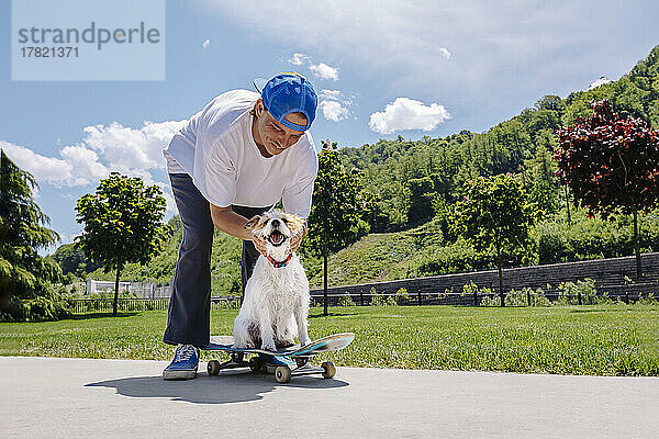 Lächelnder Mann streichelt Hund  der auf Skateboard sitzt
