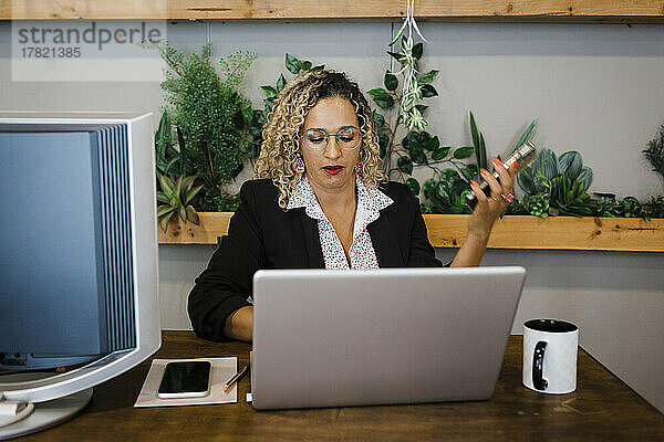 Geschäftsfrau mit Mobiltelefon und Laptop am Schreibtisch im Büro