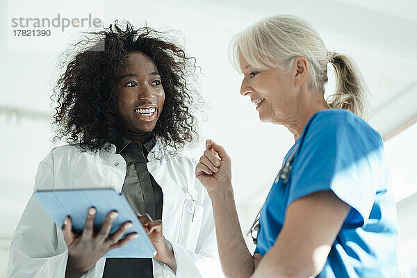 Smiling female doctor holding tablet PC talking with colleague