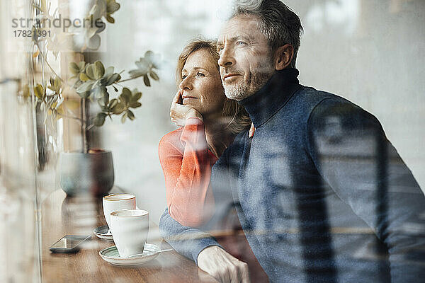 Woman sitting with head in hand by man at cafe seen through glass
