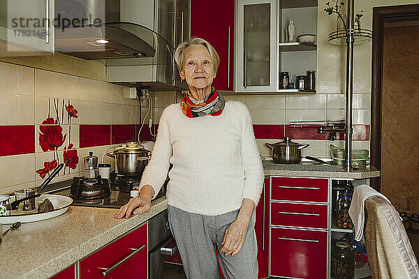 Lächelnde ältere Frau steht am Küchentisch