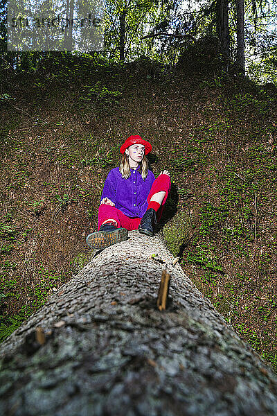 Frau mit Hut sitzt auf Baumstamm