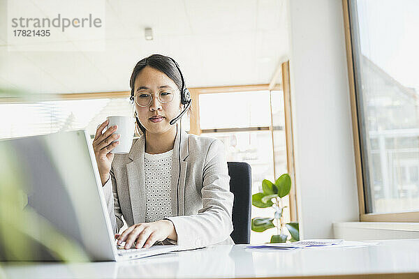 Geschäftsfrau mit Kaffeetasse arbeitet am Laptop am Schreibtisch