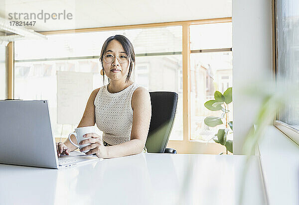 Lächelnde Geschäftsfrau mit Kaffeetasse am Schreibtisch