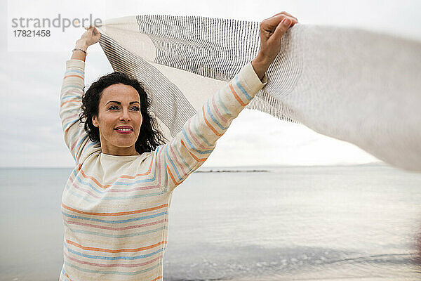 Smiling mature woman with arms raised holding scarf