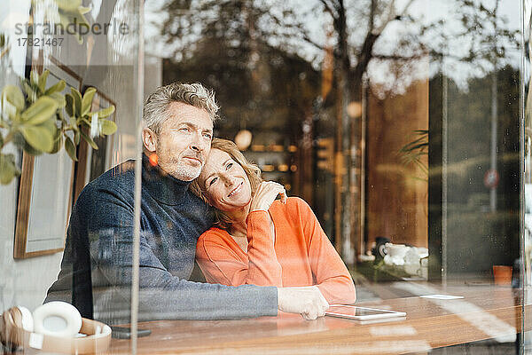Lächelnde Frau mit Mann  der im Café sitzt und durch Glas gesehen wird