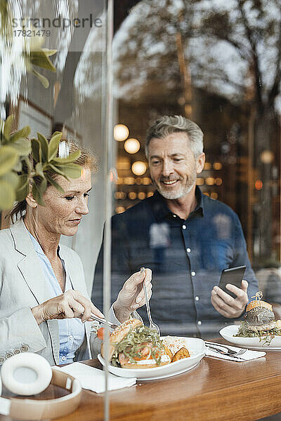 Geschäftsfrau mit Geschäftsmann hält Mobiltelefon beim Mittagessen im Café