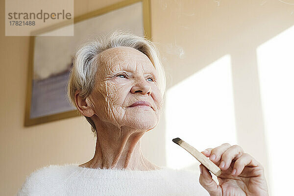Ältere Frau mit Palo-Santo-Stick zu Hause