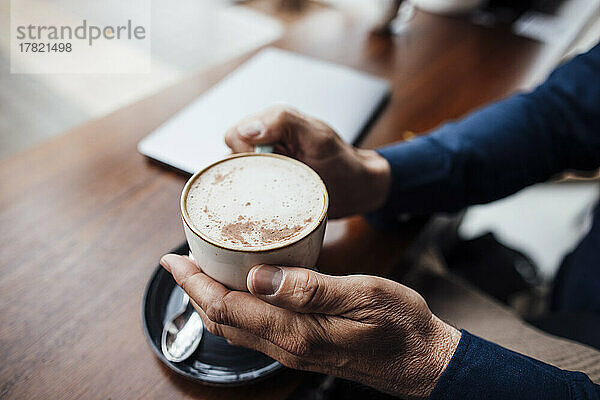 Hände eines Mannes  der eine Kaffeetasse im Café hält