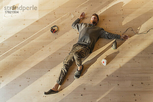 Man lying on the fresh sanded wooden floor after work. Relax under the sun in eco house