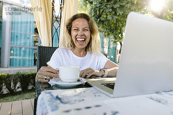 Fröhliche Frau mit Kaffeetasse am Tisch sitzend