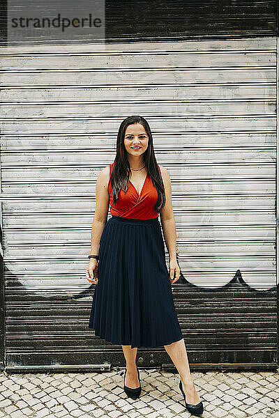 Smiling young woman standing in front of closed shutter