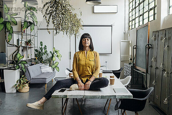 Geschäftsfrau meditiert mit geschlossenen Augen auf dem Schreibtisch im Büro