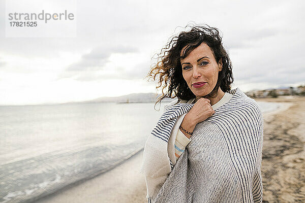 Lächelnde Frau in Schal gehüllt am Strand