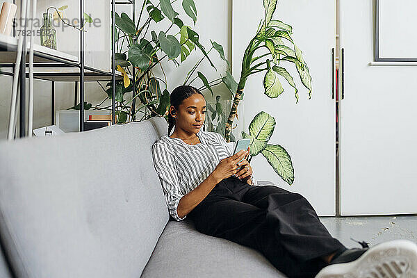 Junge Geschäftsfrau benutzt Smartphone auf Sofa im Büro
