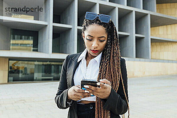 Junge Geschäftsfrau mit Mobiltelefon steht vor Bürogebäude