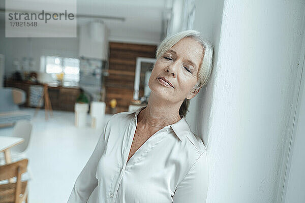 Businesswoman with eyes closed leaning on wall in office