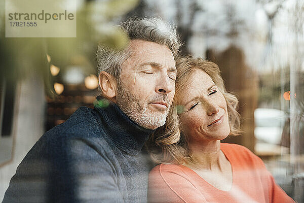 Couple with eyes closed in cafe seen through glass