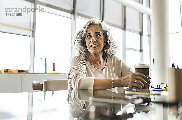 Ältere Geschäftsfrau mit Kaffeetasse sitzt am Schreibtisch