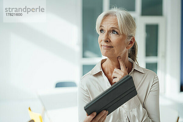 Thoughtful businesswoman holding tablet PC in office