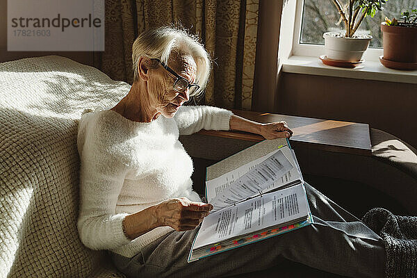 Frau mit Brille liest Dokumente und sitzt zu Hause im Wohnzimmer