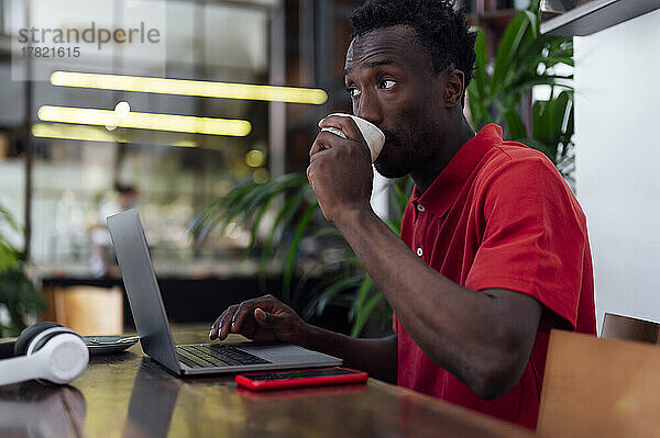 Mann trinkt Kaffee und sitzt mit Laptop im Café