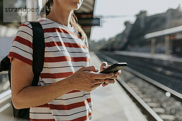 Frau benutzt Mobiltelefon am Bahnhof