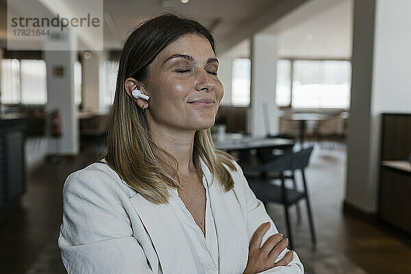Lächelnde Geschäftsfrau mit geschlossenen Augen  die im Restaurant Musik über kabellose In-Ear-Kopfhörer hört