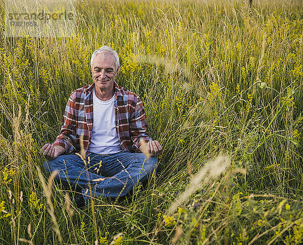 Glücklicher Bauer sitzt mit gekreuzten Beinen und meditiert inmitten von Pflanzen