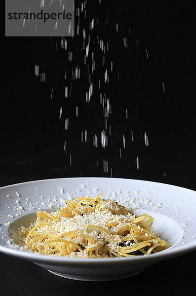 Studio shot of grated Parmesan pouring on plate of pasta