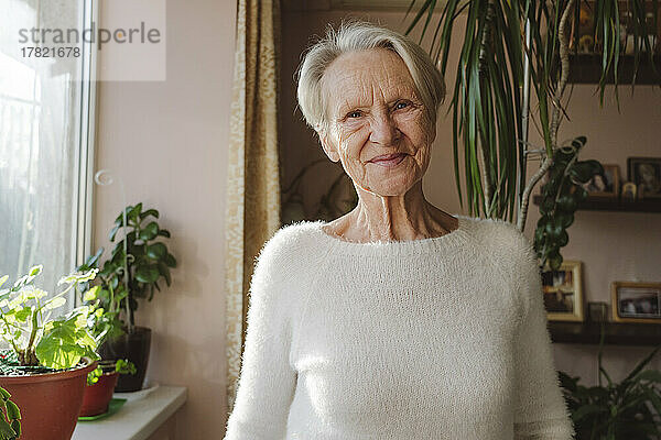 Lächelnde ältere Frau  die zu Hause vor Pflanzen steht