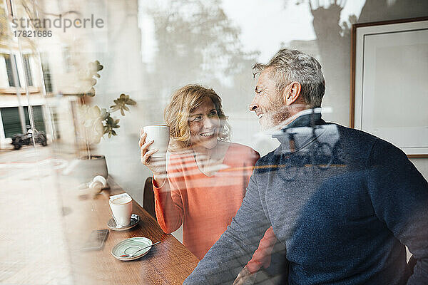 Glücklicher Mann unterhält sich mit Frau  die Kaffeetasse im Café hält