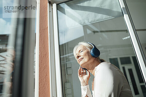 Ältere Frau mit geschlossenen Augen hört Musik über kabellose Kopfhörer