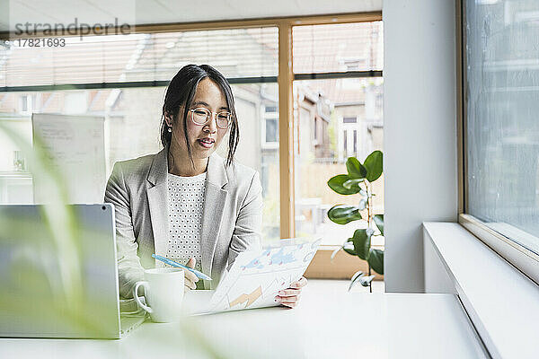Geschäftsfrau mit Brille liest Dokument im Büro