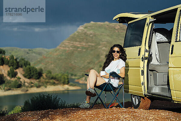 Glückliche Frau  die an einem sonnigen Tag am Van sitzt