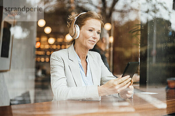 Geschäftsfrau hält Smartphone in der Hand und hört Musik im Café