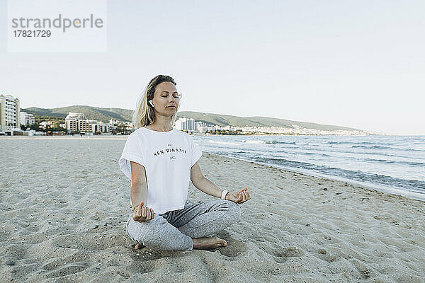 Lächelnde Frau mit geschlossenen Augen meditiert am Strand
