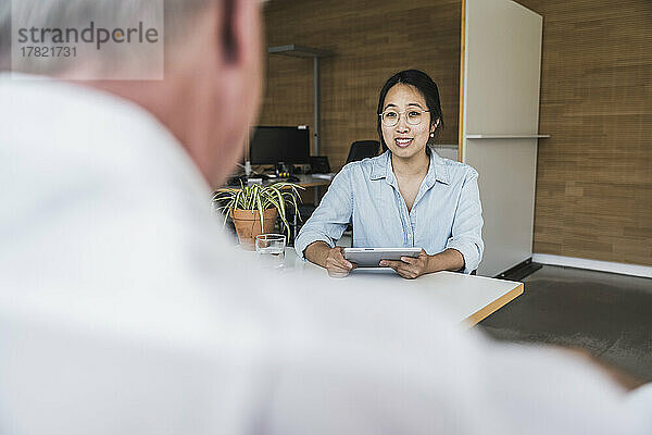 Smiling businesswoman with tablet PC discussing work at desk