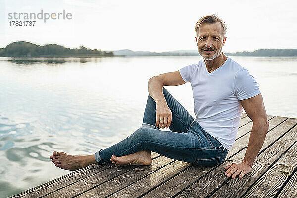 Lächelnder reifer Mann sitzt auf dem Steg am See