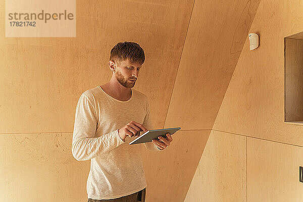 Mann richtet eine Smart-Home-Einheit mit digitalem Tablet in einem Öko-Haus ein