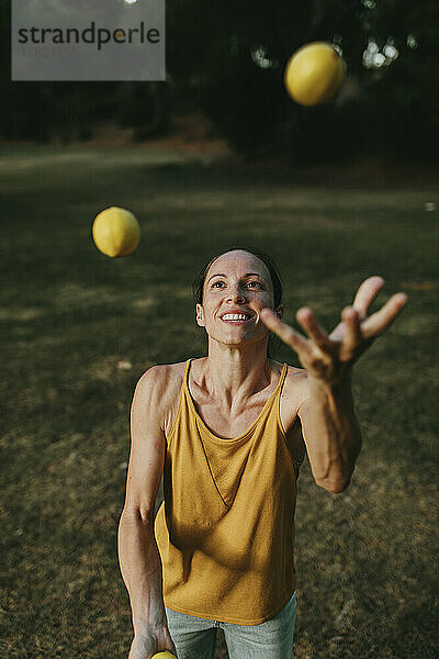 Lächelnde Frau jongliert mit Zitronen im Park