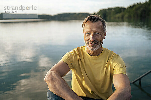 Glücklicher reifer Mann  der an einem sonnigen Tag vor dem See sitzt