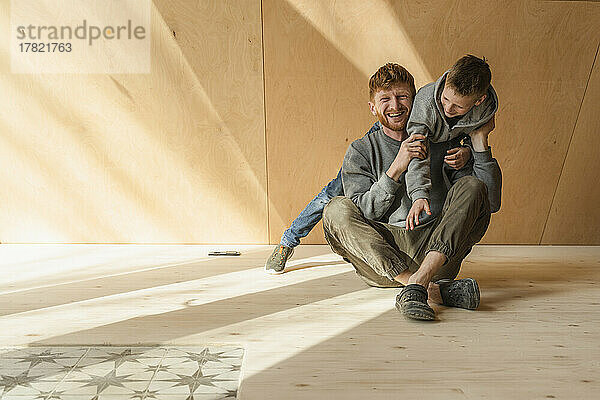 Father and son play fighing on the floor in wooden eco house