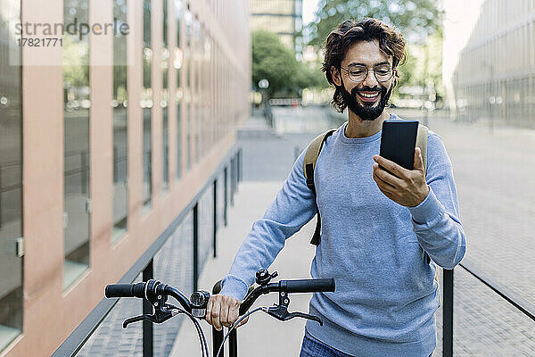 Lächelnder Mann mit Fahrrad  der in der Stadt telefoniert