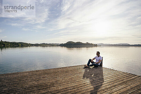 Reifer Mann sitzt auf dem Pier am See
