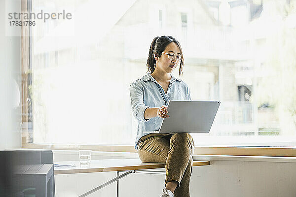 Businesswoman working on laptop by window at work place